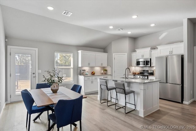 kitchen with light stone counters, light hardwood / wood-style flooring, an island with sink, stainless steel appliances, and white cabinets