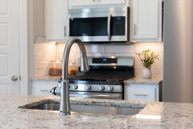 kitchen with white cabinetry, light stone countertops, sink, and backsplash