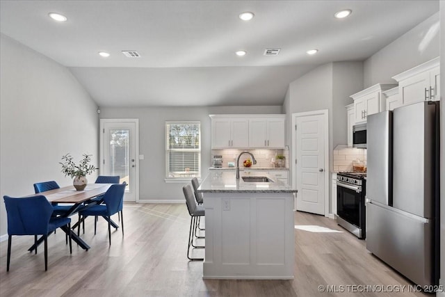 kitchen with sink, stainless steel appliances, light stone counters, an island with sink, and white cabinets