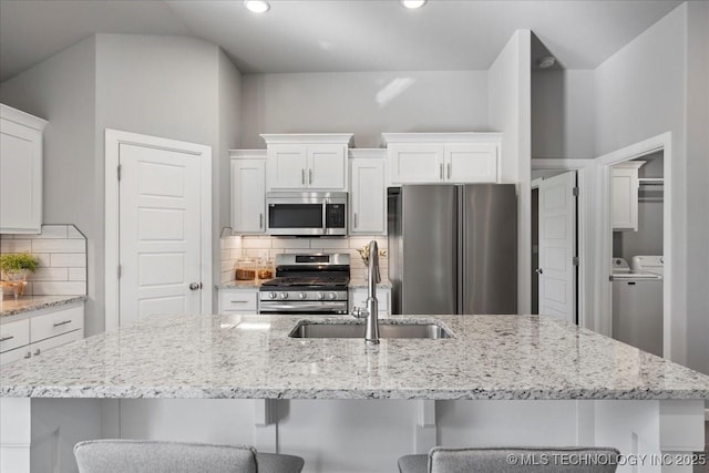 kitchen with white cabinetry, a breakfast bar, stainless steel appliances, and washer and clothes dryer