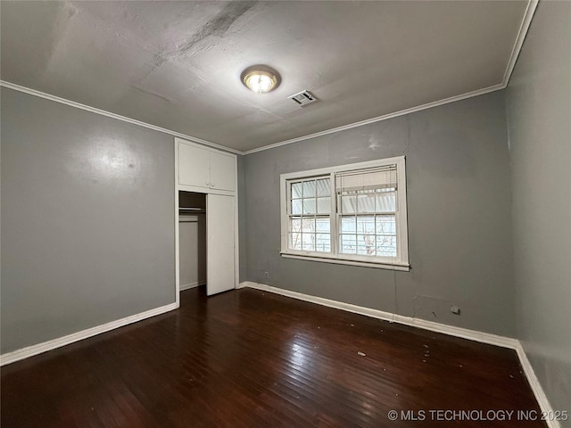 unfurnished bedroom with dark wood-type flooring, crown molding, and a closet