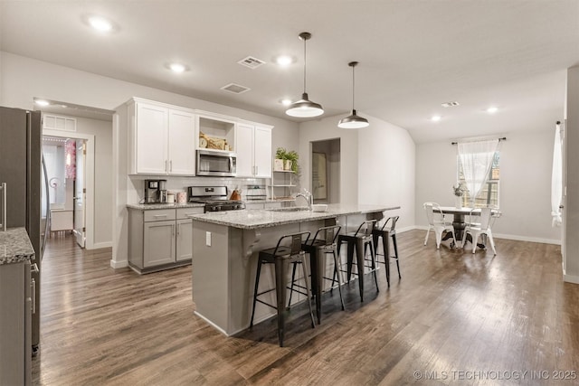 kitchen featuring white cabinetry, a kitchen breakfast bar, hanging light fixtures, stainless steel appliances, and a center island with sink