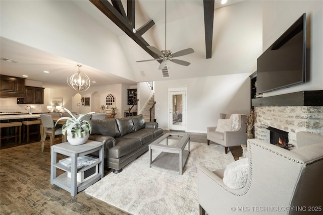 living room with wood-type flooring, high vaulted ceiling, beamed ceiling, a fireplace, and ceiling fan with notable chandelier