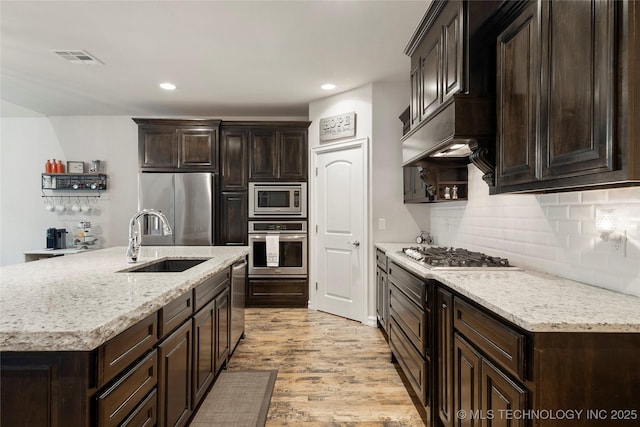 kitchen featuring sink, light hardwood / wood-style flooring, stainless steel appliances, dark brown cabinetry, and decorative backsplash