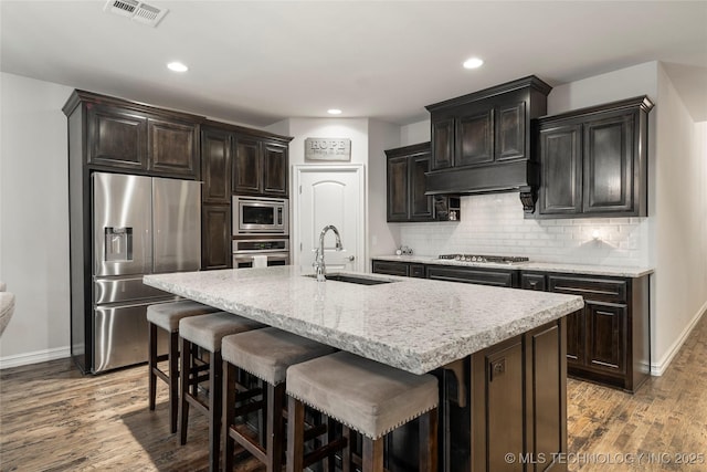 kitchen featuring sink, a kitchen island with sink, stainless steel appliances, light hardwood / wood-style floors, and decorative backsplash