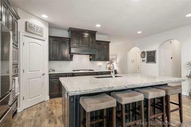 kitchen featuring stainless steel gas cooktop, dark hardwood / wood-style floors, sink, and a center island with sink