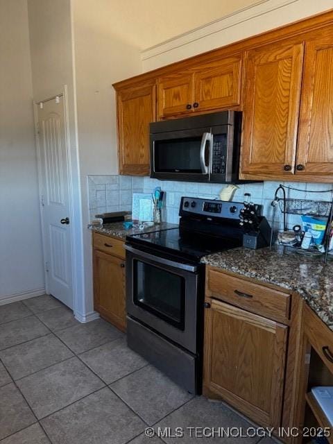 kitchen with light tile patterned flooring, dark stone countertops, backsplash, and stainless steel electric range