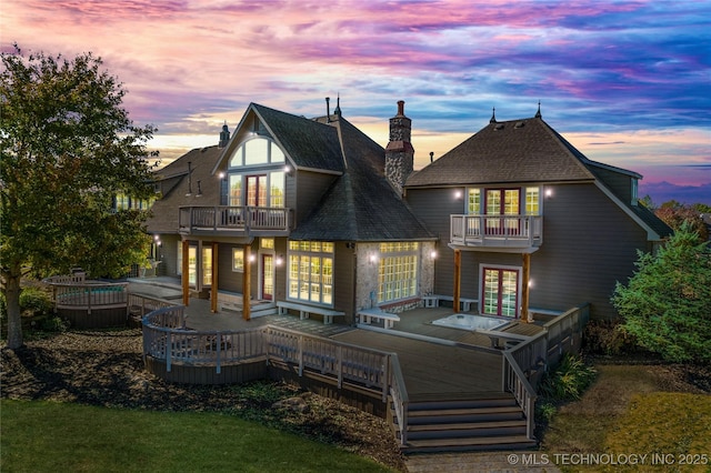 back house at dusk with a wooden deck and a balcony