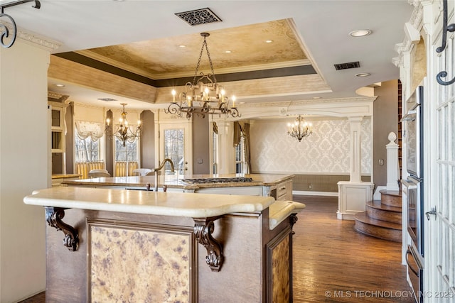 kitchen featuring hanging light fixtures, ornamental molding, a notable chandelier, a raised ceiling, and a center island with sink