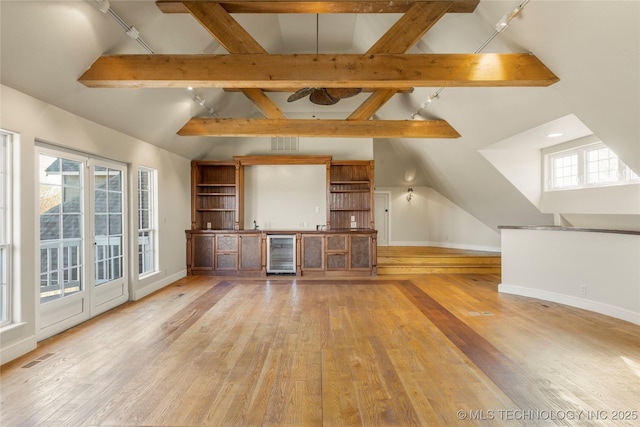 unfurnished living room with beverage cooler, a wealth of natural light, light wood-type flooring, and vaulted ceiling with beams