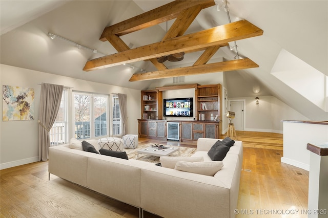 living room featuring rail lighting, vaulted ceiling with beams, bar, and light wood-type flooring