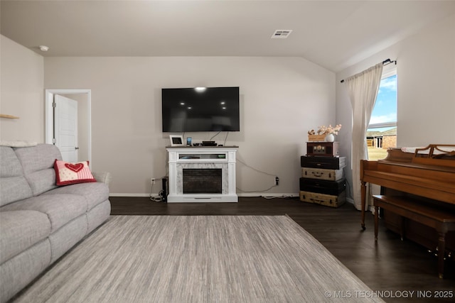 living area featuring dark wood-style flooring, a fireplace, lofted ceiling, visible vents, and baseboards