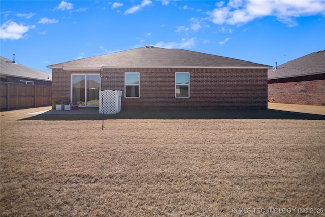 rear view of property featuring a shingled roof, brick siding, a yard, and fence