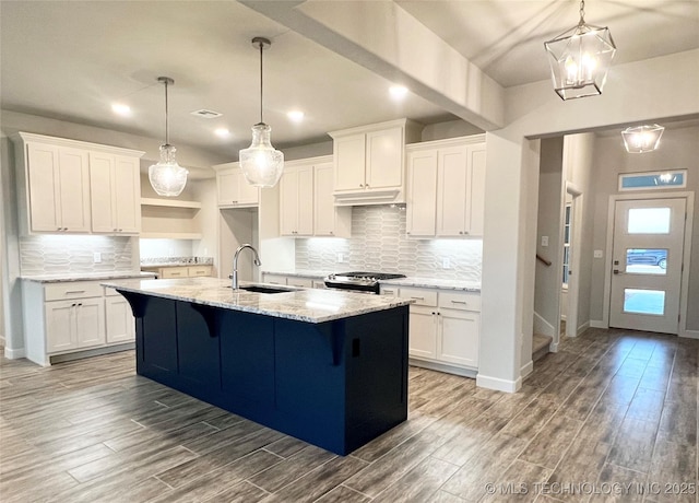 kitchen featuring sink, stainless steel gas stove, light stone counters, a kitchen island with sink, and white cabinets