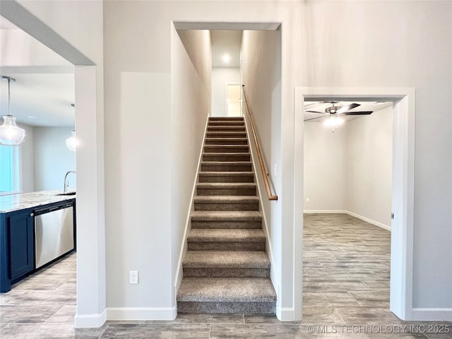 staircase with ceiling fan, sink, and hardwood / wood-style floors