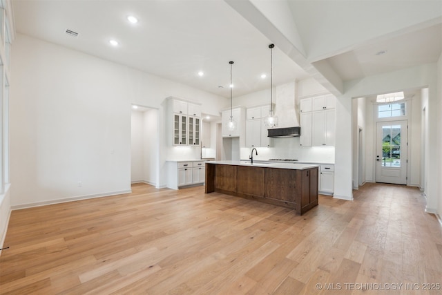2722 E 134th Cir, Bixby, OK 74008 - kitchen with custom exhaust hood, light wood-type flooring, white cabinets, an island with sink, and stovetop