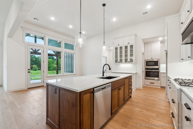 2722 E 134th Cir, Bixby, OK 74008 - kitchen with appliances with stainless steel finishes, an island with sink, light wood-style flooring, white cabinetry, and glass insert cabinets