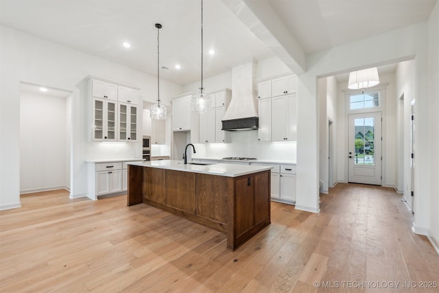 2722 E 134th Cir, Bixby, OK 74008 - kitchen with premium range hood, gas cooktop, light wood-style flooring, a center island with sink, and white cabinets
