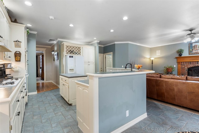 kitchen featuring ornamental molding, a kitchen island with sink, ceiling fan, a brick fireplace, and white appliances