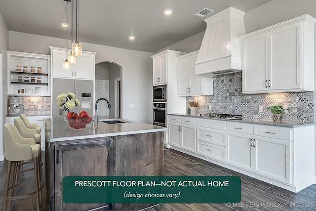 kitchen featuring premium range hood, decorative light fixtures, white cabinets, oven, and a kitchen island with sink