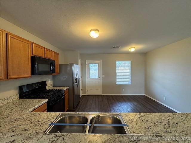 kitchen featuring dark wood-type flooring, sink, light stone counters, a textured ceiling, and black appliances