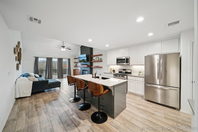 kitchen with sink, appliances with stainless steel finishes, a kitchen breakfast bar, a kitchen island with sink, and white cabinets