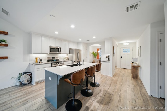 kitchen with sink, appliances with stainless steel finishes, backsplash, white cabinets, and a kitchen bar