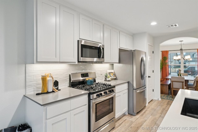 kitchen featuring light hardwood / wood-style flooring, an inviting chandelier, backsplash, stainless steel appliances, and white cabinets