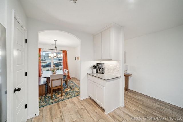 kitchen featuring white cabinetry, decorative light fixtures, light hardwood / wood-style flooring, and backsplash