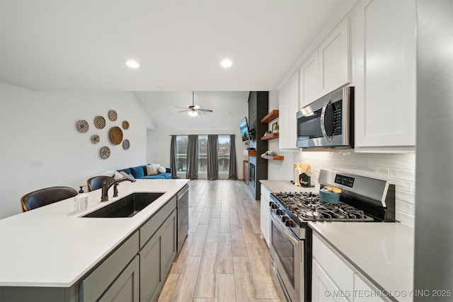 kitchen with sink, appliances with stainless steel finishes, tasteful backsplash, white cabinets, and a center island with sink