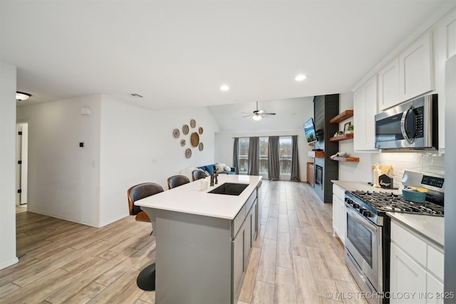 kitchen featuring sink, appliances with stainless steel finishes, white cabinetry, a kitchen breakfast bar, and a center island with sink