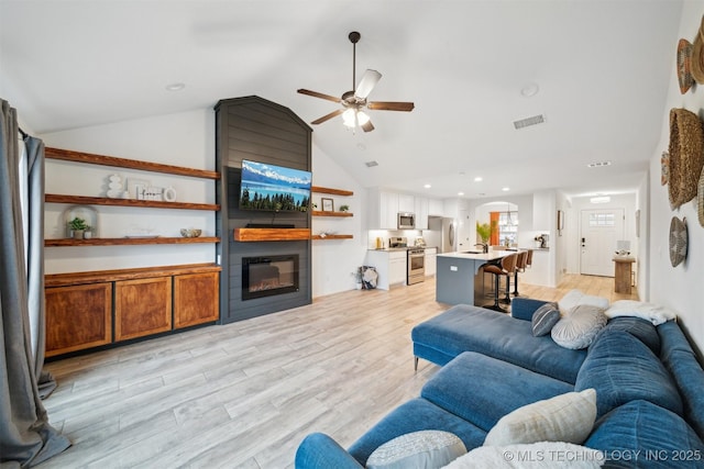 living room with ceiling fan, lofted ceiling, a fireplace, and light hardwood / wood-style flooring