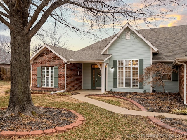 ranch-style house featuring brick siding, roof with shingles, and a lawn