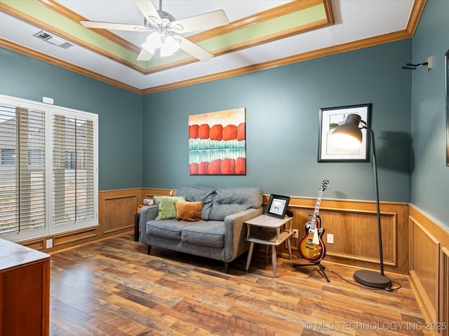 living area featuring hardwood / wood-style floors, visible vents, ornamental molding, and a wainscoted wall