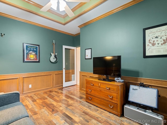 living room featuring ornamental molding, a ceiling fan, wainscoting, wood finished floors, and french doors