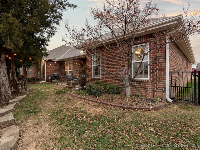 view of home's exterior featuring brick siding, fence, and a yard