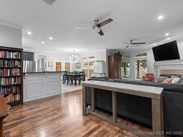 living area featuring ceiling fan with notable chandelier, wood finished floors, ornamental molding, and recessed lighting