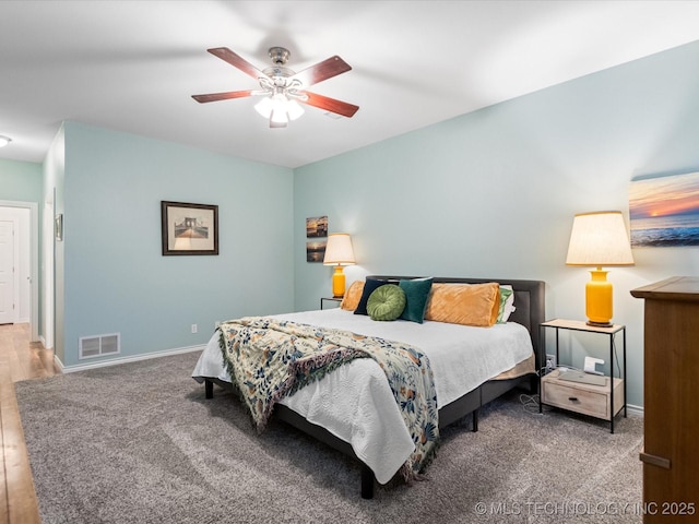 carpeted bedroom featuring visible vents, baseboards, a ceiling fan, and wood finished floors