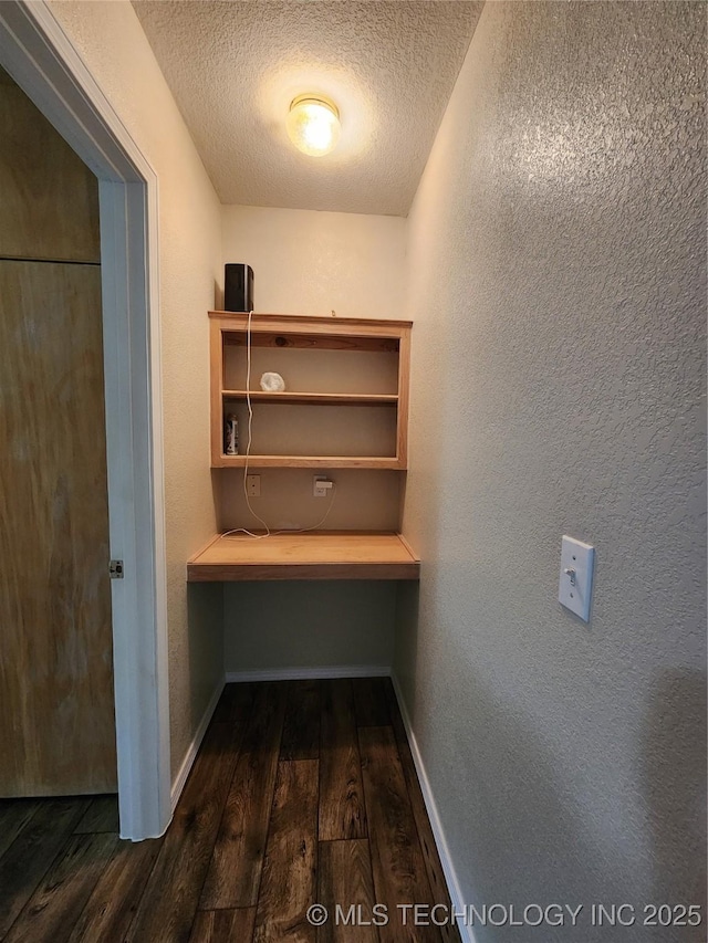 interior space featuring dark wood-type flooring, built in desk, and a textured ceiling