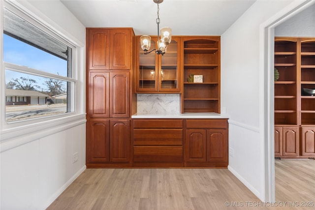 interior space featuring light hardwood / wood-style flooring, an inviting chandelier, hanging light fixtures, decorative backsplash, and built in shelves