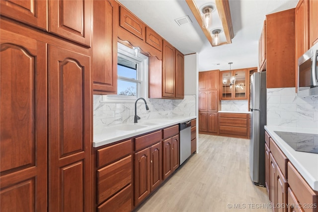 kitchen with sink, decorative light fixtures, light wood-type flooring, stainless steel appliances, and backsplash