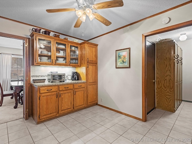 kitchen with ornamental molding, light tile patterned floors, backsplash, and light stone counters