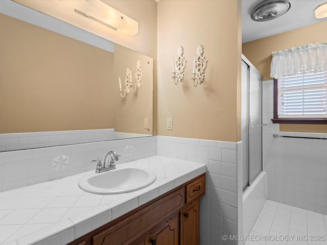 bathroom featuring vanity, combined bath / shower with glass door, tile walls, and a textured ceiling