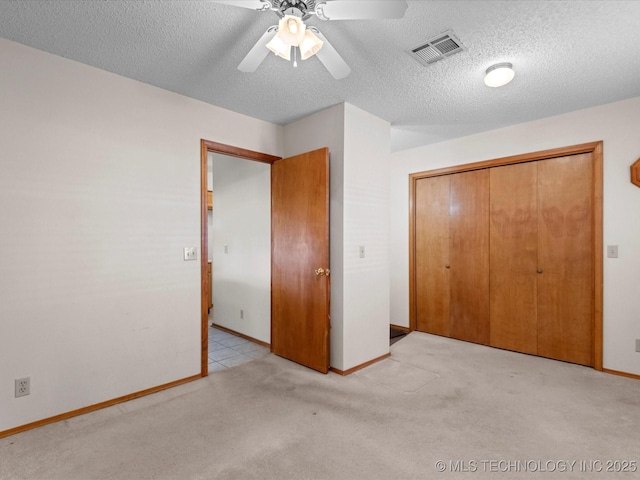 unfurnished bedroom featuring ceiling fan, a closet, light carpet, and a textured ceiling