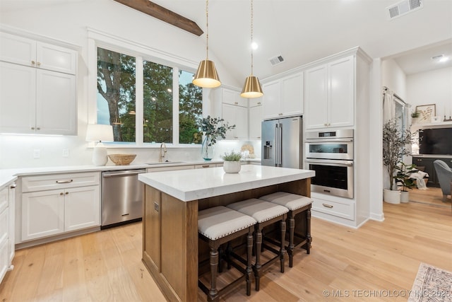 2325 E 134th Cir, Bixby, OK 74008 - kitchen featuring appliances with stainless steel finishes, light wood-type flooring, white cabinets, a kitchen island, and vaulted ceiling