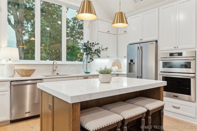 2325 E 134th Cir, Bixby, OK 74008 - kitchen with stainless steel appliances, a center island, light wood-type flooring, white cabinets, and decorative light fixtures