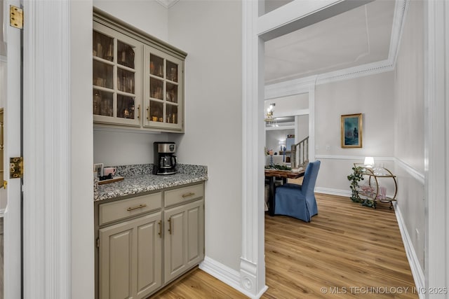 bar featuring ornamental molding, light stone countertops, and light wood-type flooring