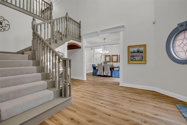 entryway with crown molding, a towering ceiling, a chandelier, and hardwood / wood-style floors