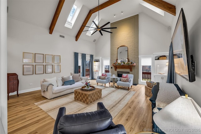 living room with light hardwood / wood-style flooring, beam ceiling, a skylight, and high vaulted ceiling