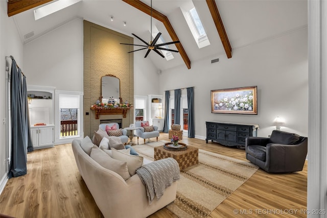 living room featuring a fireplace, a skylight, high vaulted ceiling, and light hardwood / wood-style floors